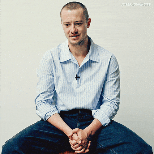 a man in a blue striped shirt is sitting with his hands out