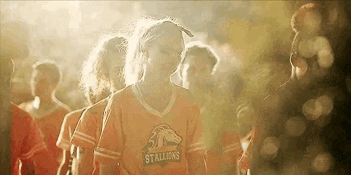 a group of young girls are standing next to each other in a row wearing orange jerseys .