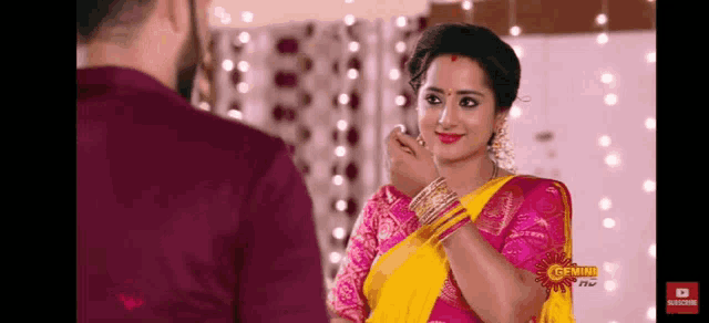 a woman in a yellow and pink saree is standing next to a man in a purple shirt .