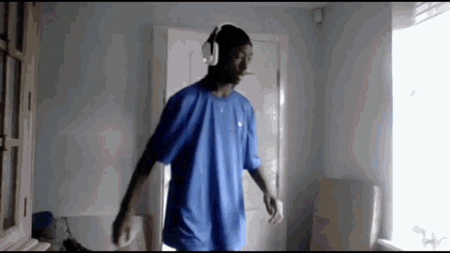 a man wearing headphones and a blue shirt is dancing in a room