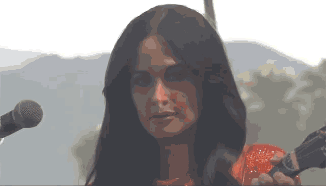 a woman in a red dress is singing into a microphone with mountains in the background