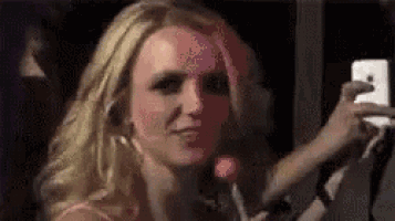 a blonde woman is taking a selfie with a lollipop in her mouth .