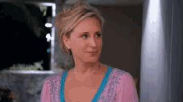 a woman in a pink sweater and blue shirt is standing in front of a window .
