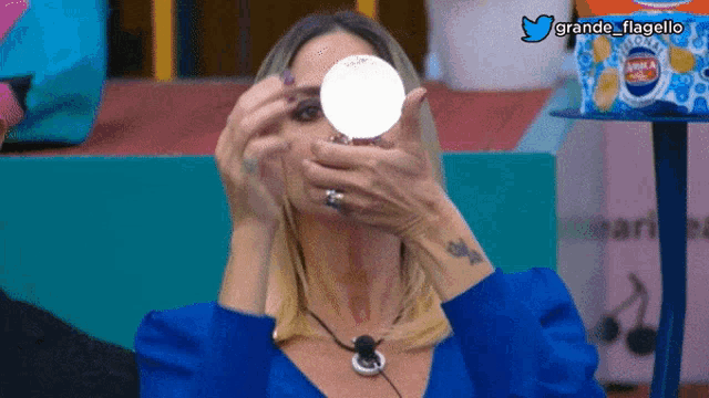 a woman in a blue shirt is holding a white object in front of her face and the words grande flagello are on the bottom of the image