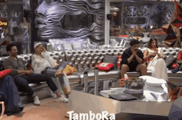 a group of people are sitting on a couch in a room with the word tambora written on the floor