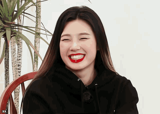 a woman wearing a black hoodie and red lipstick laughs