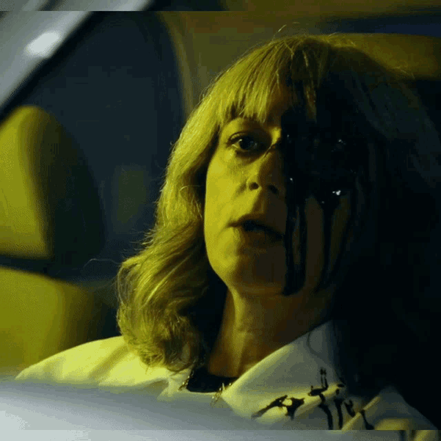 a woman with blood dripping from her face is wearing a white shirt with the letter t on it