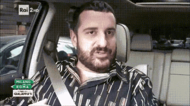 a man with a beard is sitting in the back seat of a car with a seat belt on .