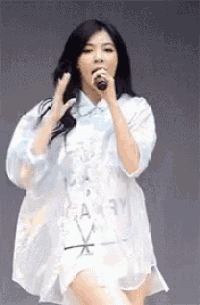 a woman in a white dress is holding a microphone and singing into it .