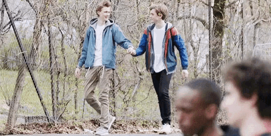 two young men are holding hands while walking down the street .