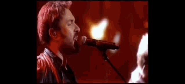 a man singing into a microphone with a guitar in the background