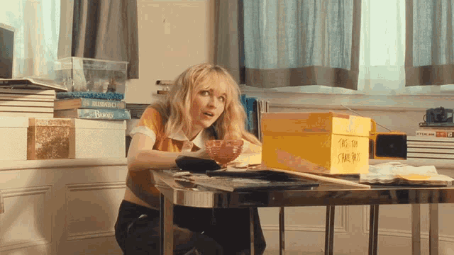 a woman sits at a table with a yellow box on it that says ' this on '