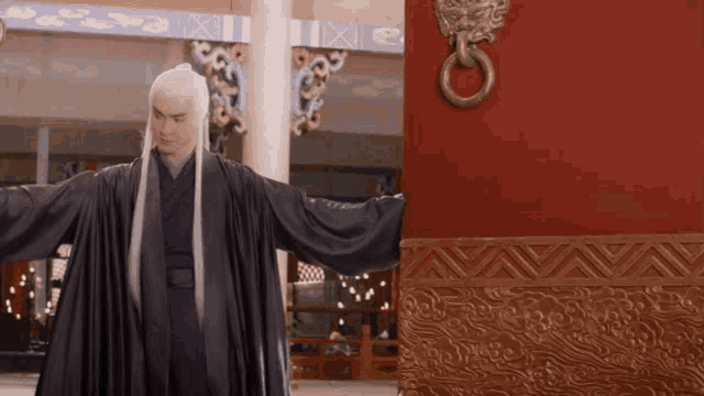 a man with long white hair is standing in front of a door