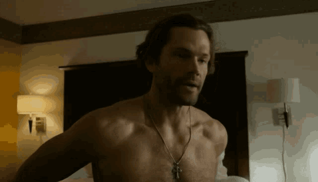 a man without a shirt is standing in a bedroom