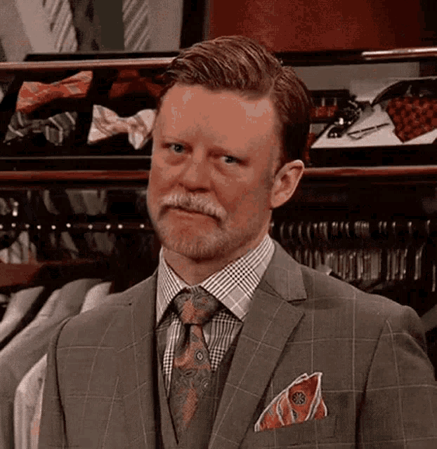 a man in a suit and tie is standing in front of a display of ties and bow ties .