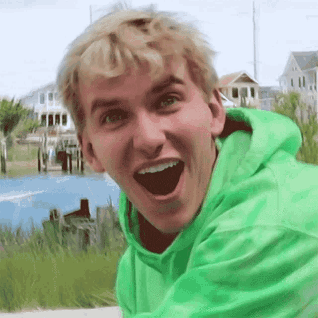 a young man in a green hoodie is smiling with his mouth open