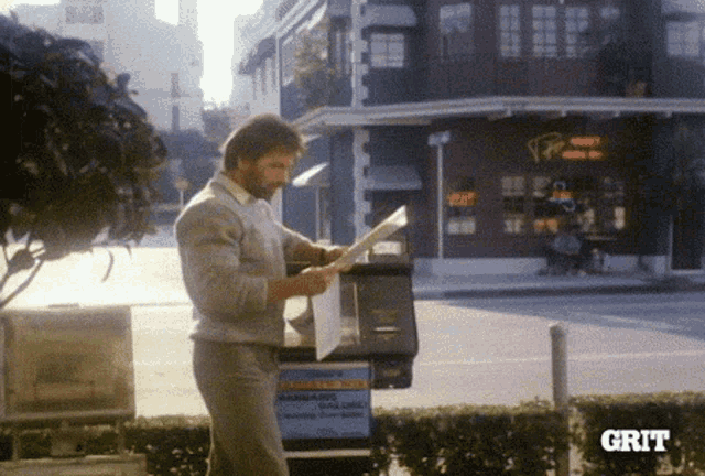 a man is reading a newspaper in front of a building with the word grit on the bottom right