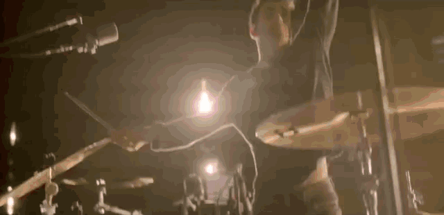 a man is singing into a microphone in a dark room while playing drums .
