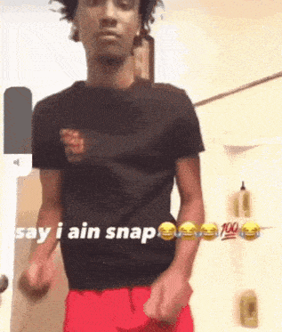 a man in a black shirt and red shorts is standing in front of a door and saying say i ain snap .