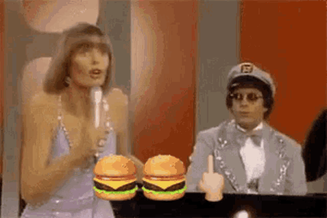 a woman is singing into a microphone while a man is sitting at a piano with two hamburgers .