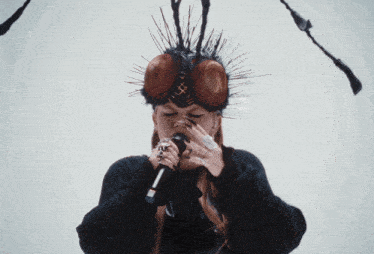 a woman with a fly on her head singing into a microphone