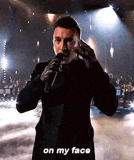 a man in a suit is singing into a microphone on a stage and says `` on my face '' .