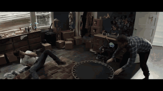 two men playing with a trampoline in a room with boxes