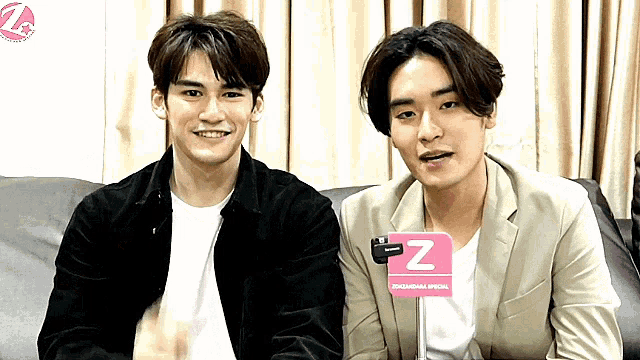 two young men are sitting next to each other on a couch with a pink sign that says z on it