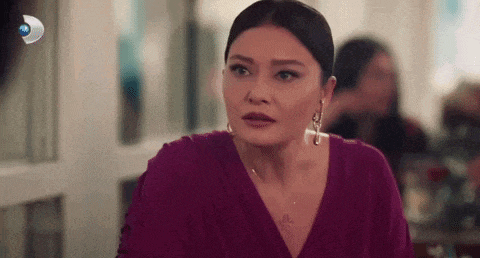 a woman in a purple dress and earrings is sitting at a table looking at the camera .