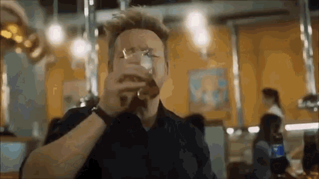 a man in a black shirt is drinking a glass of beer