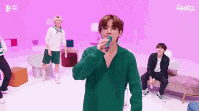 a man in a green sweater is singing into a microphone in a room with other people .