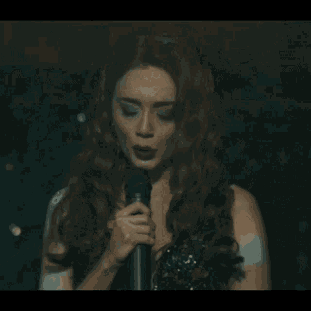 a woman with long hair is singing into a microphone in a dark room