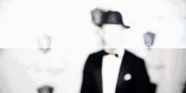 a man in a tuxedo and fedora is standing in front of a white wall