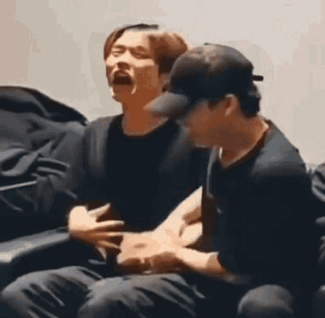 two men are sitting next to each other on a couch and one of them is holding the other 's belly .