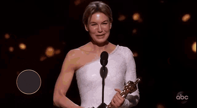 a woman in a white dress stands in front of a microphone with the words best actress 2020 written on the bottom