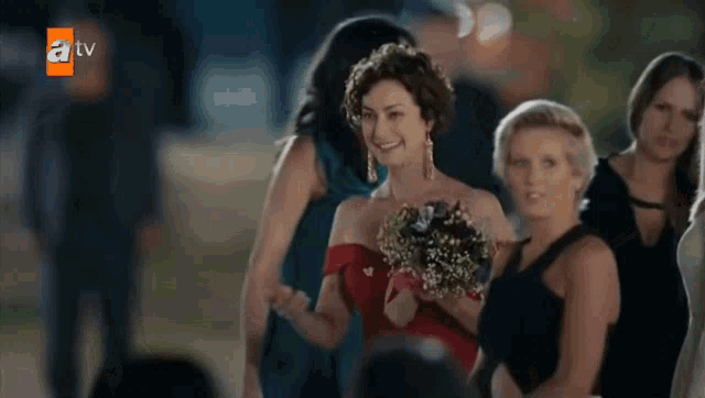 a woman in a red dress is holding a bouquet of flowers in front of a tv logo
