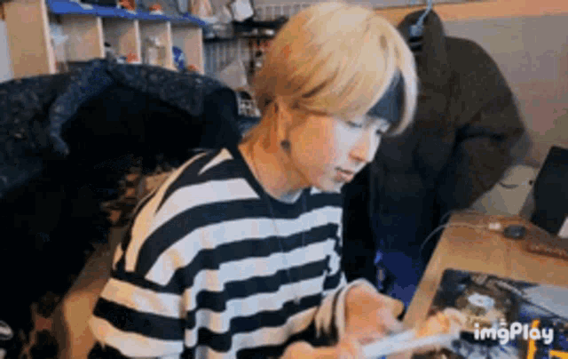 a person wearing a striped shirt is sitting at a table using a tablet