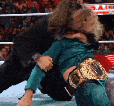 a man in a suit is holding a woman in a wrestling ring who is wearing a gold belt
