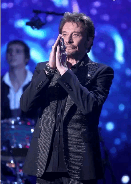a man in a black suit is clapping his hands