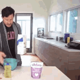 a man is standing in a kitchen preparing food with a bowl and a bag of yogurt .