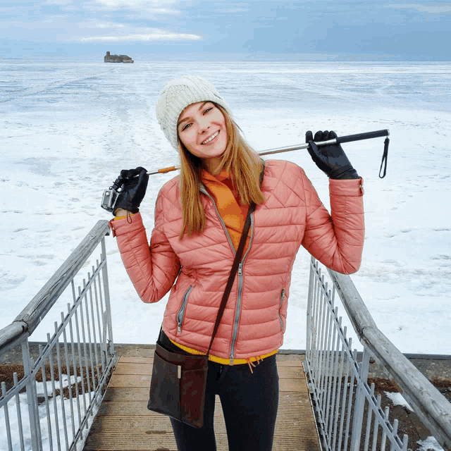 a woman in a pink jacket holds a camera and a pole