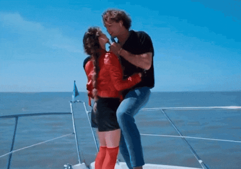 a man and a woman kissing on a boat in the ocean