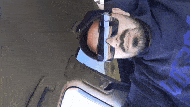 a man wearing sunglasses and a blue shirt with the letter c on it is laying down in a car