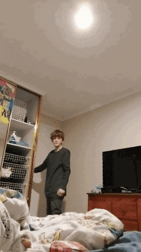 a boy is standing in a bedroom with a tv and a closet