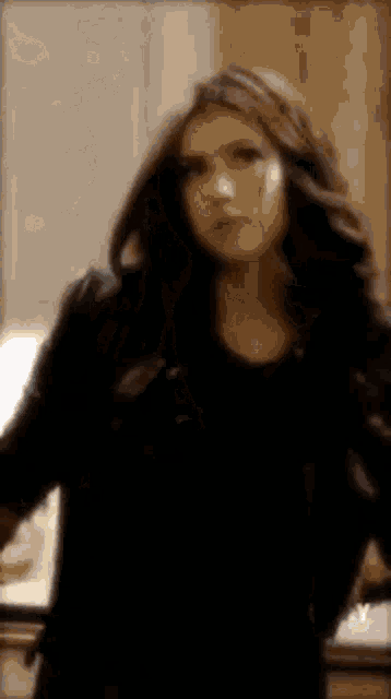 a woman in a black jacket is standing in front of a mirror in a room .
