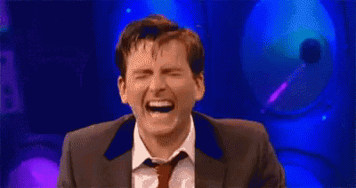 a man in a suit and tie is laughing with his eyes closed on a stage .