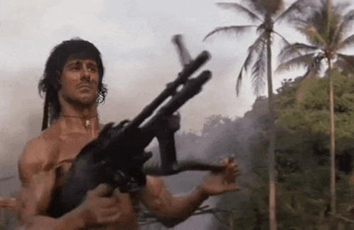 a shirtless man is holding a gun in a forest .