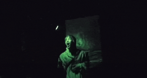 a person is standing in a dark room with a green light coming out of the corner .