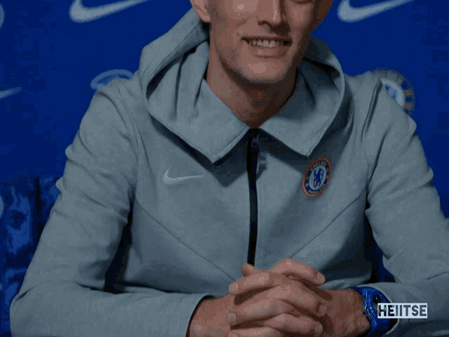 a man wearing a grey nike jacket with a chelsea logo on it