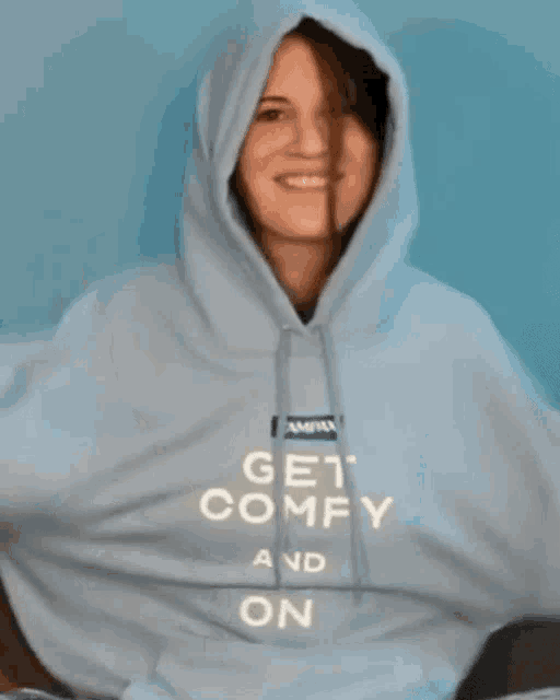 a woman wearing a light blue hoodie is smiling and looking at the camera